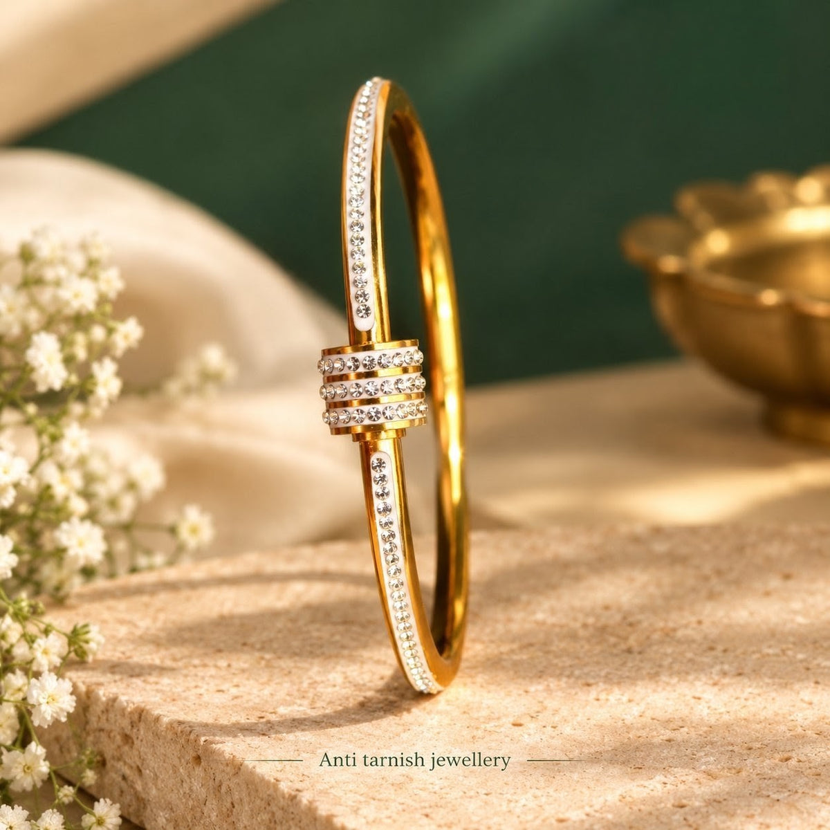 Close-up of a golden hinged bangle bracelet featuring a triple crystal-encrusted center ring and paved crystal sides, resting on a textured surface.