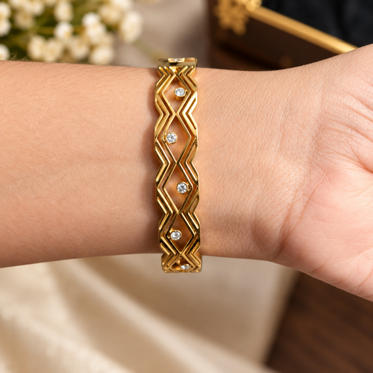 Close-up of a golden geometric zigzag bangle bracelet featuring scattered crystal accents worn on a wrist.