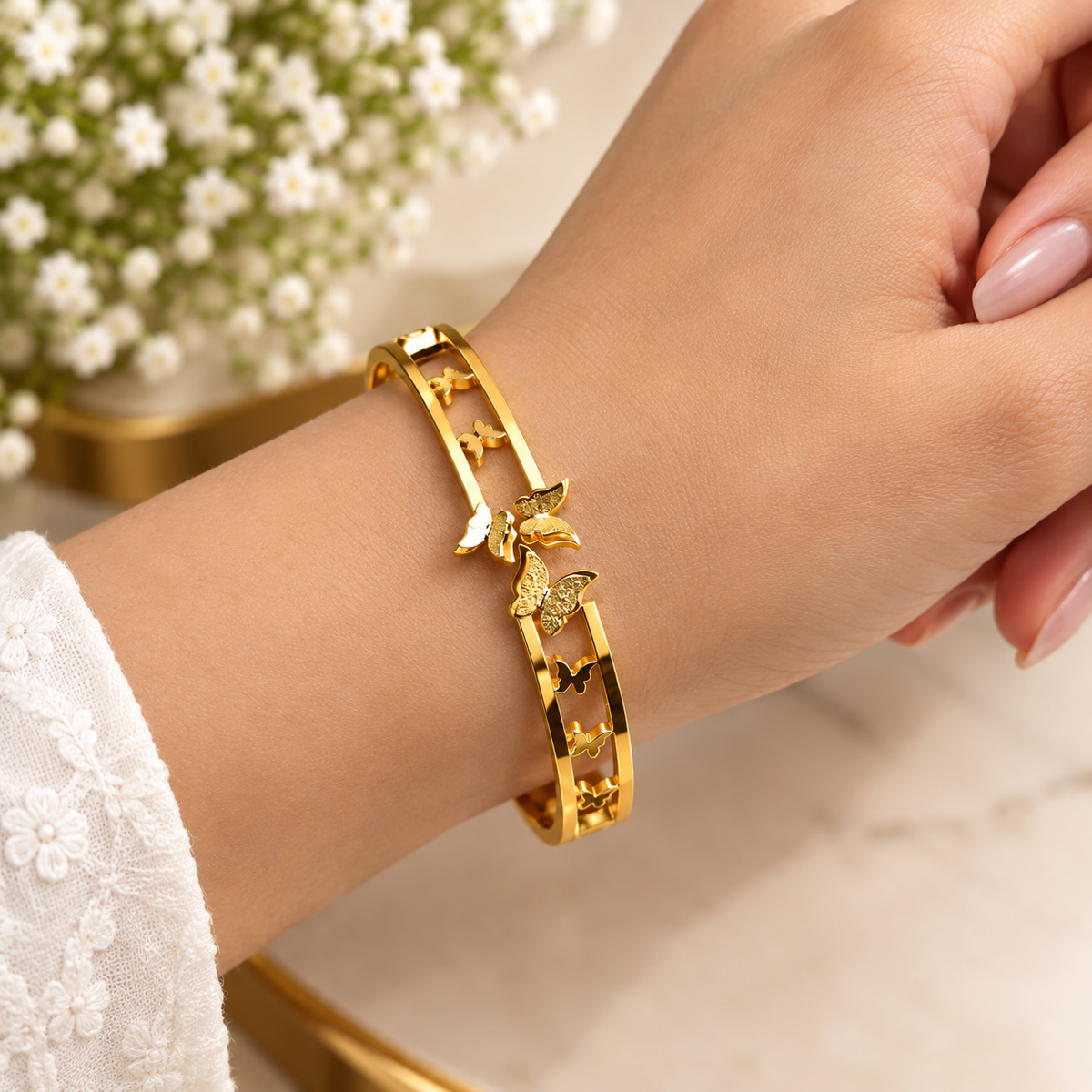Close-up of a golden open cuff bracelet featuring a cut-out track design with charming butterfly accents worn on a wrist.