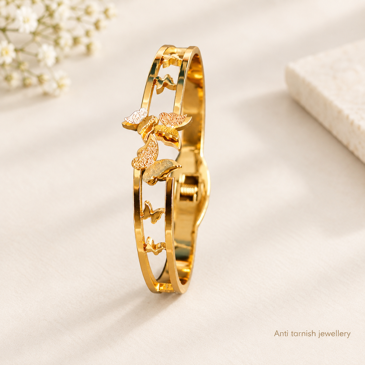 Close-up of a golden open cuff bracelet featuring a cut-out track design with charming butterfly accents worn on a wrist.