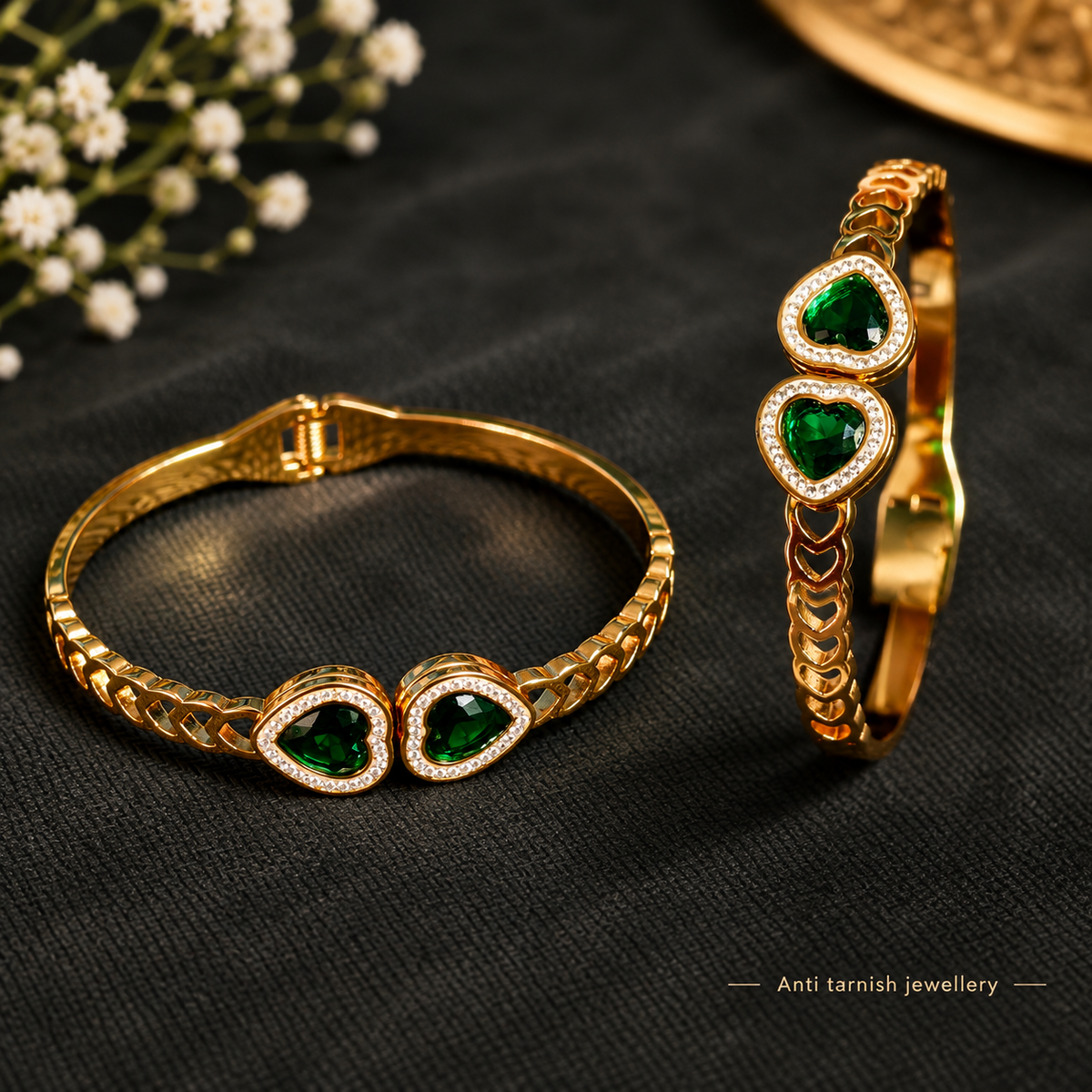 Close-up shot of a wrist wearing a golden chain bracelet with dual green heart-shaped gemstones and sparkling pave halos.