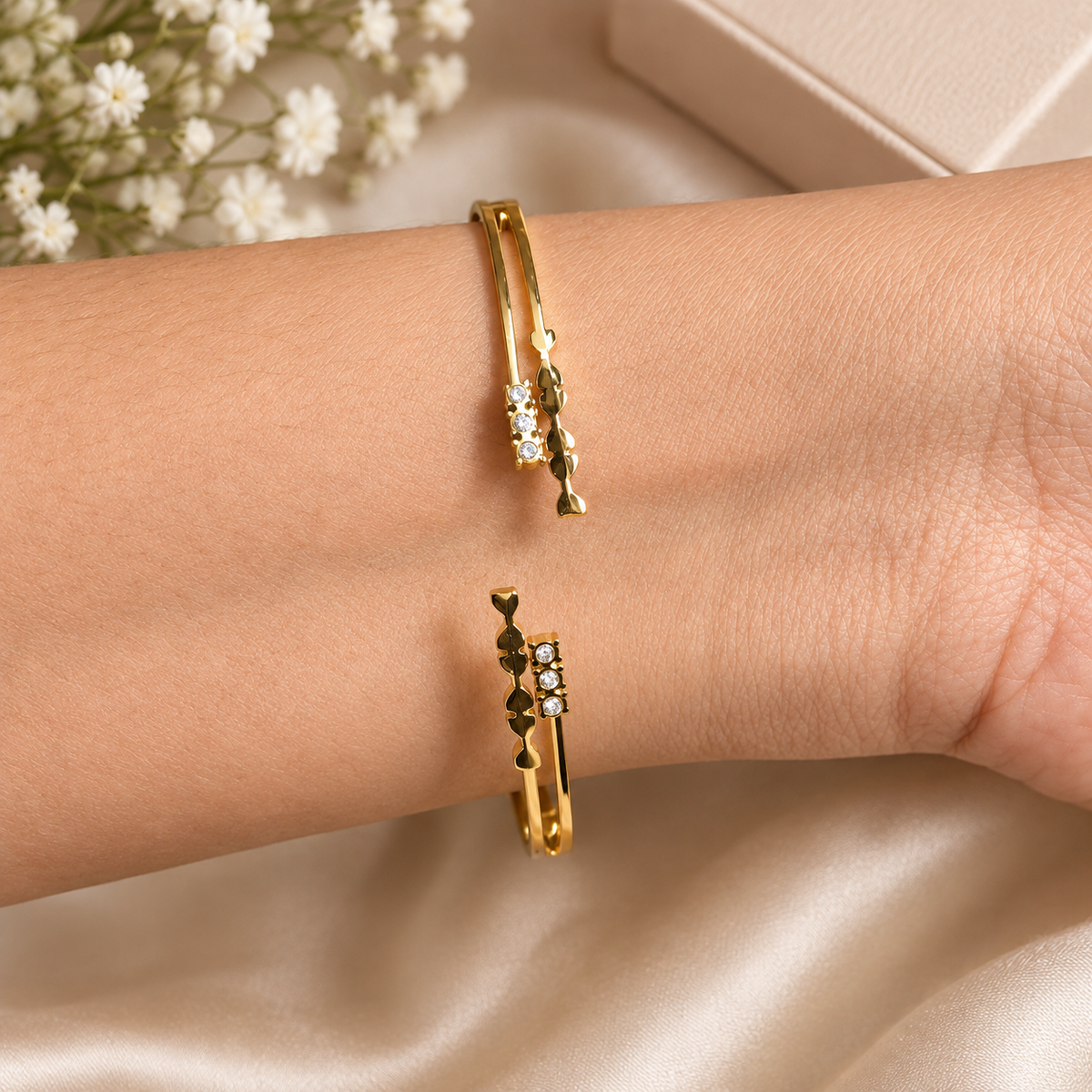 Close-up of a golden double-band open cuff bracelet featuring crystal stones and heart motifs worn on a wrist.