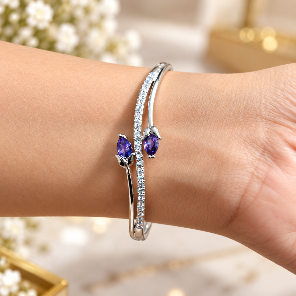 Close-up of a silver-tone open cuff bracelet featuring twin purple crystal tulip buds and a pave crystal accent band worn on a wrist.