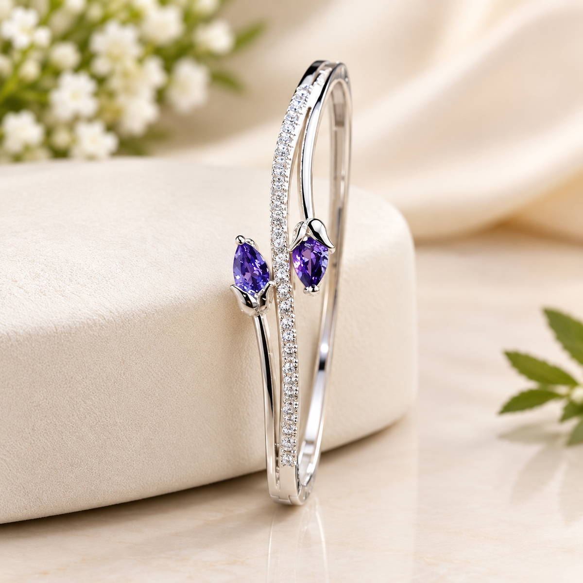 Studio product shot of a silver-tone open cuff bracelet featuring two vibrant purple pear-cut crystals styled as tulip buds alongside a shimmering pave crystal band, resting on a neutral padded surface.