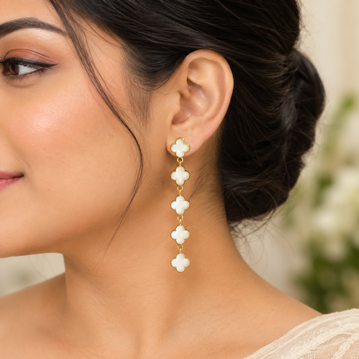 Close-up profile of a woman wearing elegant long gold and white clover drop earrings.   