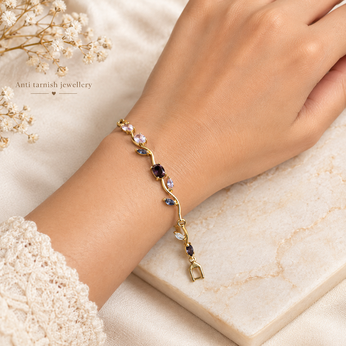 Woman's wrist wearing an anti-tarnish winding vine bracelet with purple and blue stones, resting on a white marble surface