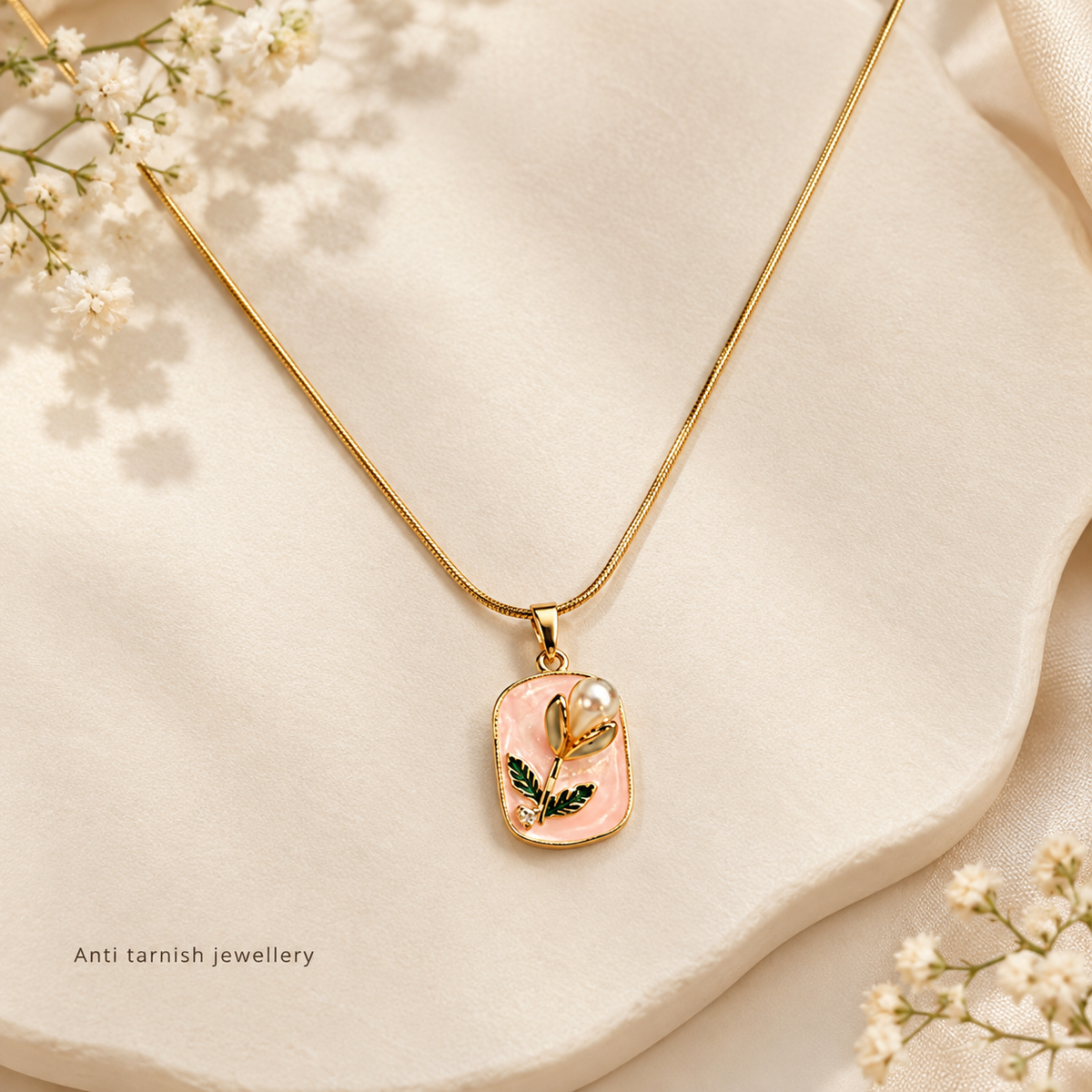 Golden anti tarnish necklace with a blush pink botanical pendant, green leaf details, sculpted flower bud, and pearl accent